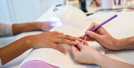 close-up-beautician-painting-woman-s-nails-with-brush-nail-salon